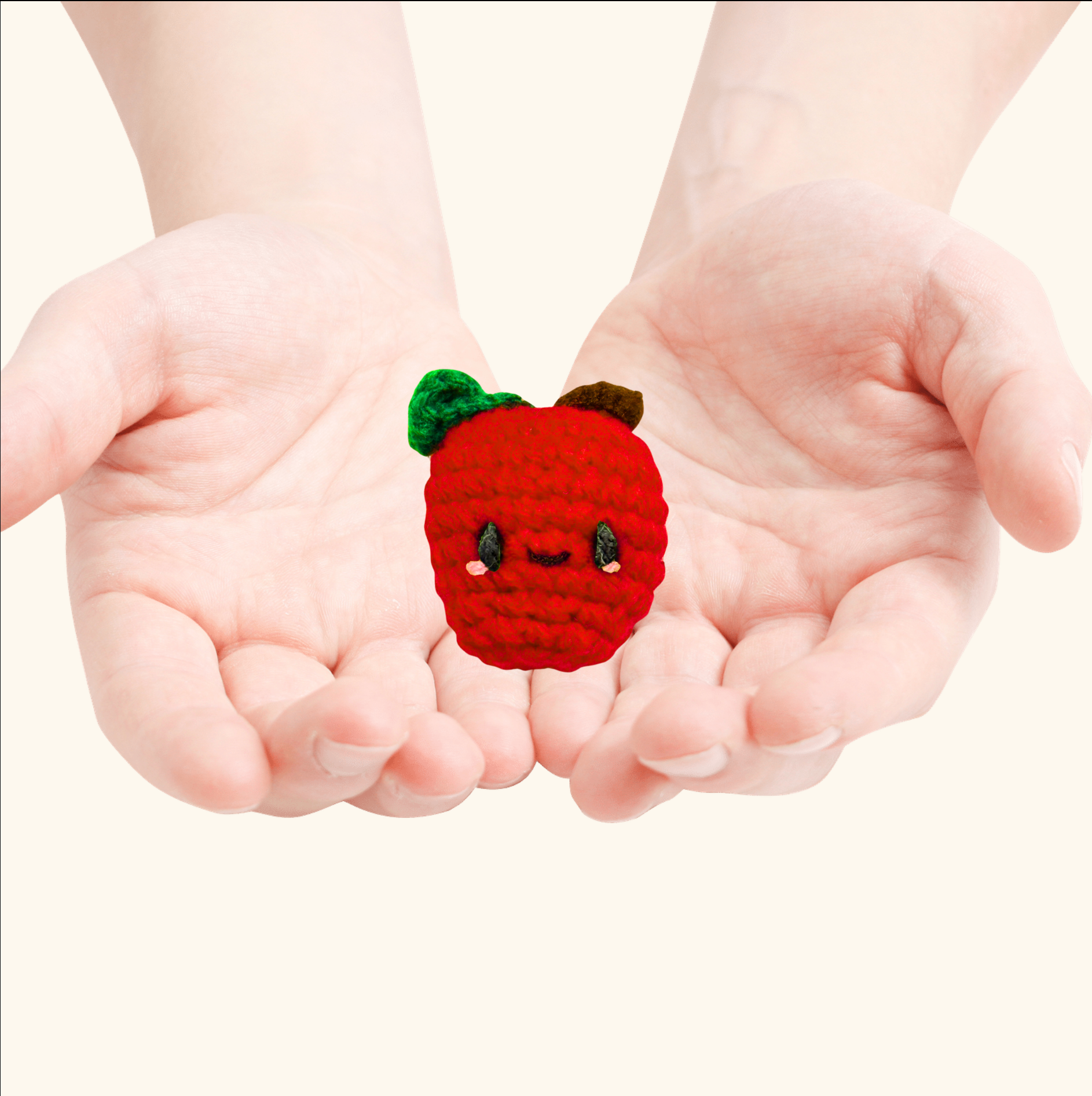Small red crocheted apple with a face held between two hands against a white background to represent an apple shaped Chunkle catnip toy infused with Miracle Nip botanicals by Minou Le-Mew