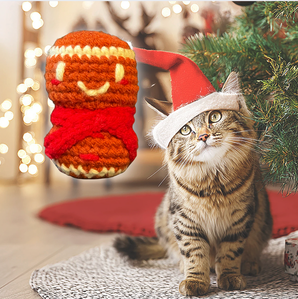 Cat wearing a Santa hat next to a Christmas-themed cat toy with a blurred festive background to represent Minou Le-Mew artisan Chunkle catnip toy infused with Miracle Nip botanicals