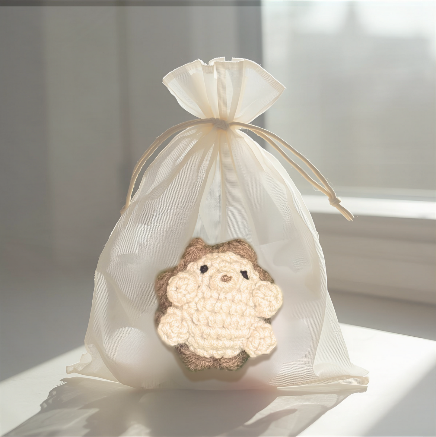 Crocheted hedgehog toy in a white drawstring bag on a light surface.
