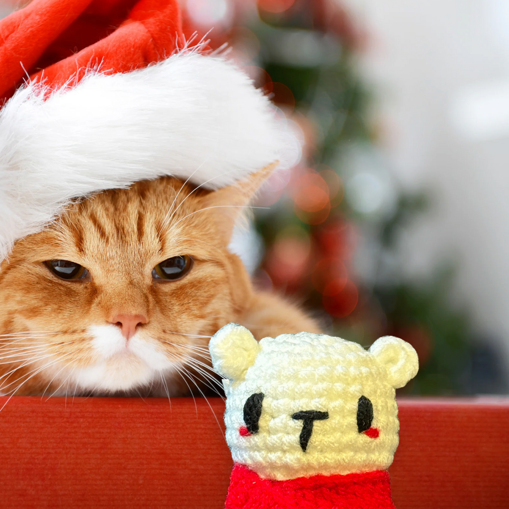 Cat wearing a Santa hat with a small plush cat toy in front of it, Christmas tree in the background to represent Chunkle catnip toy infused with Miracle Nip botanicals by Minou Le-Mew