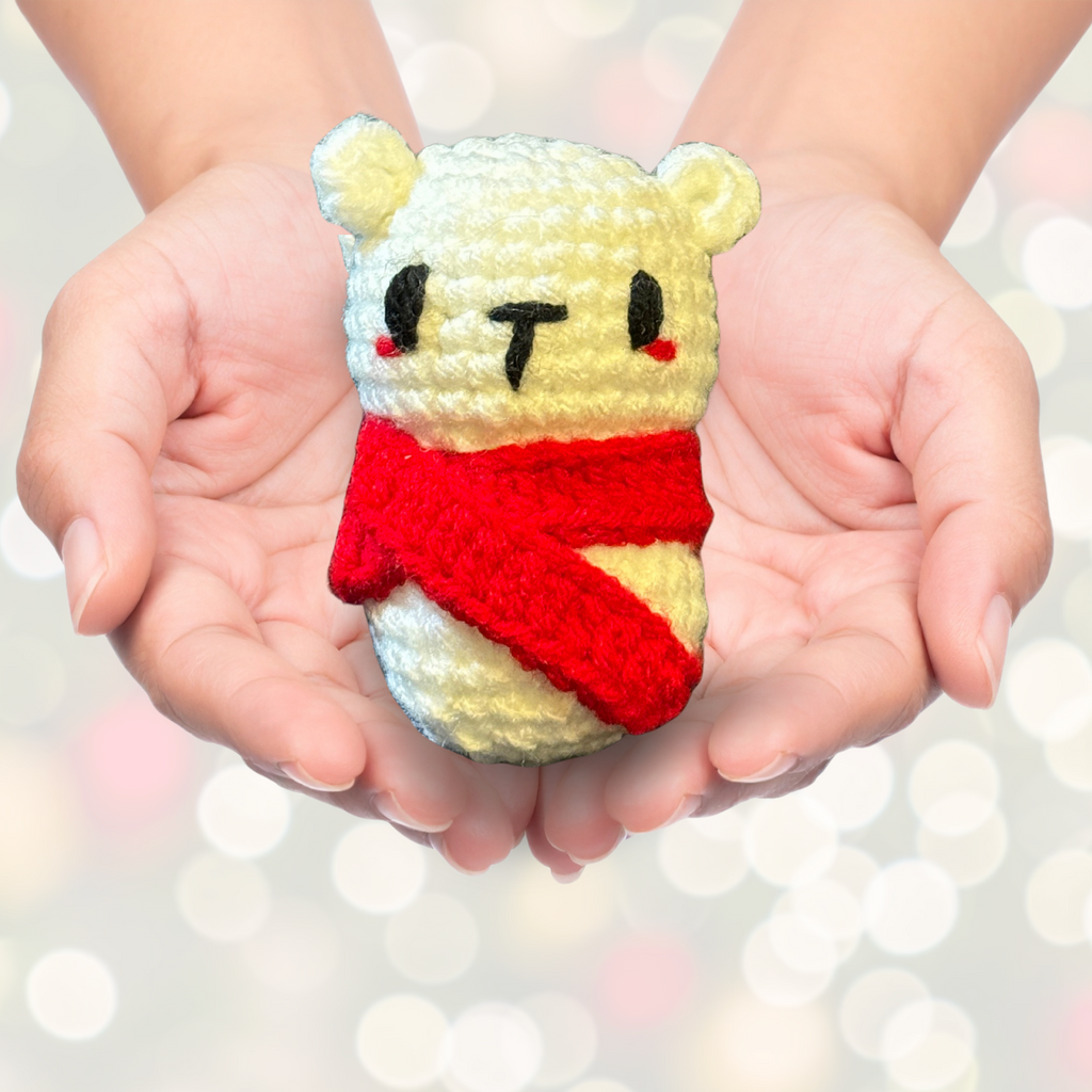Handmade crochet polar bear Christmas cat toy with a red scarf held in hands against a blurred light background to represent Artisan Chunkle catnip toy from Minou Le-Mew infused with Miracle Nip botanicals