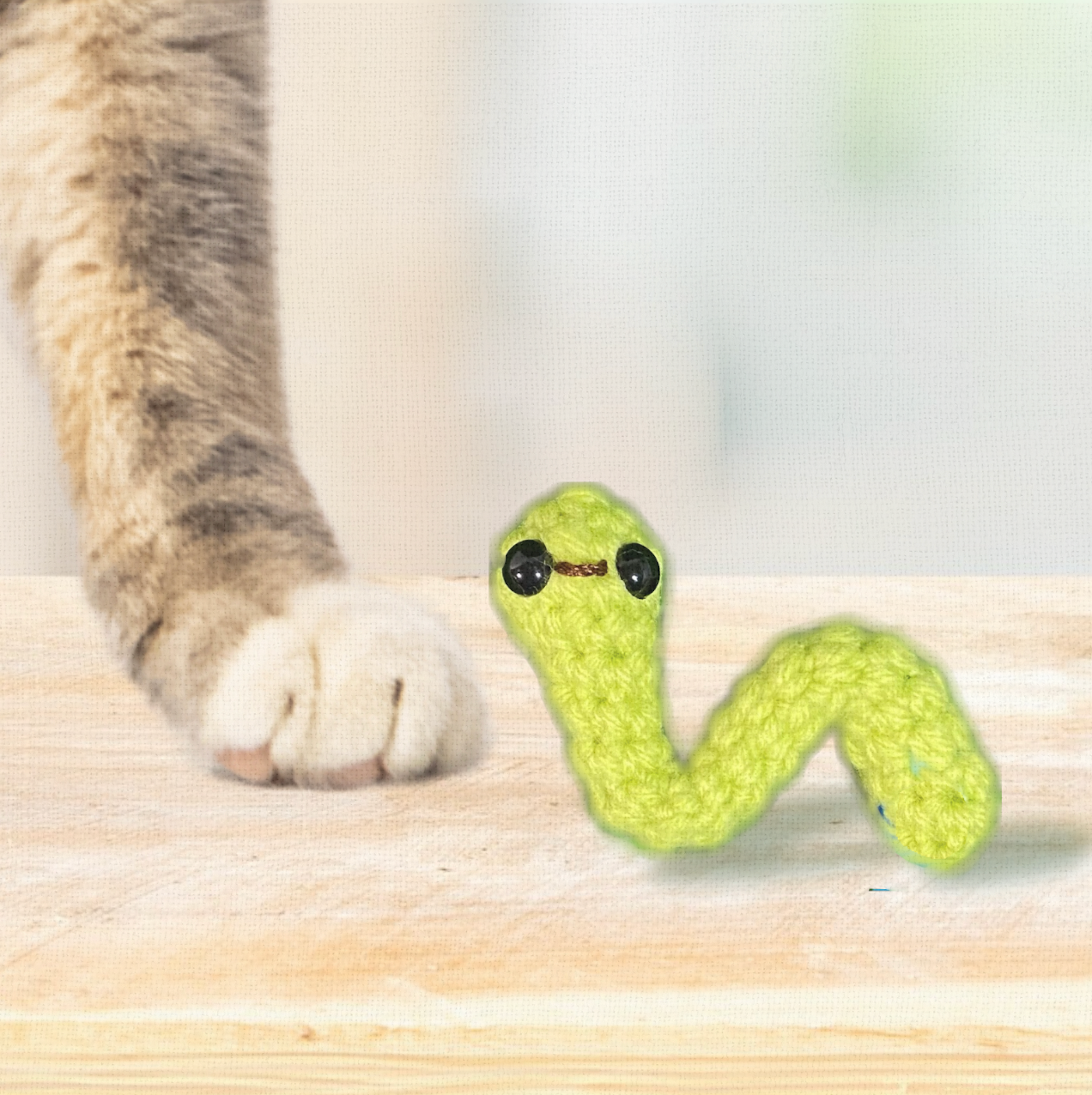 Noodle the Inchworm, a 3.5 inch handmade catnip toy by Feline Grove, shown beside a hand for scale. The elongated woven body highlights petite yet durable design.