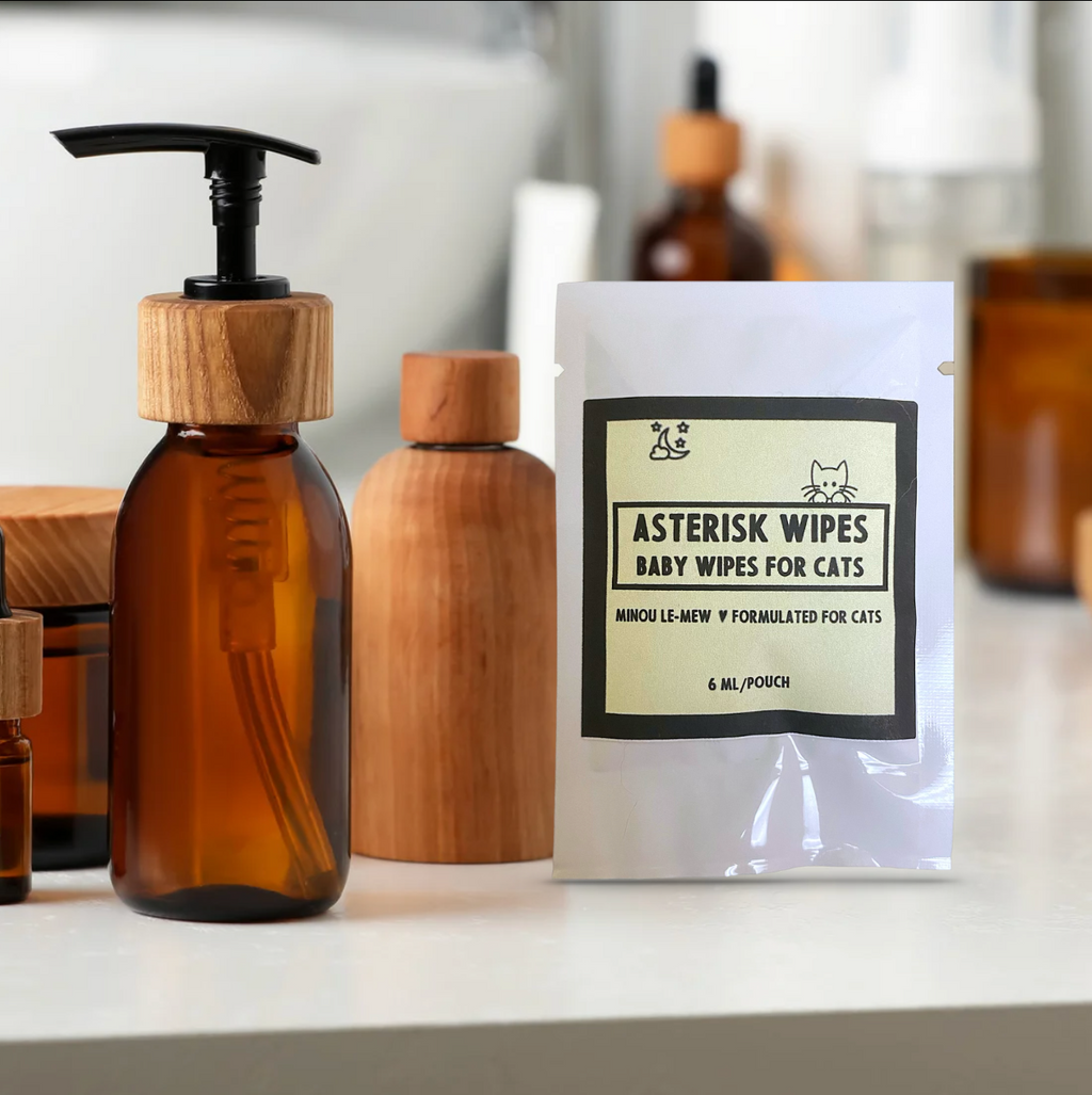 Asterisk Wipes by Minou Le-Mew arranged with other amber bottles and grooming products. Boutique cat hygiene essentials for the elegant home.