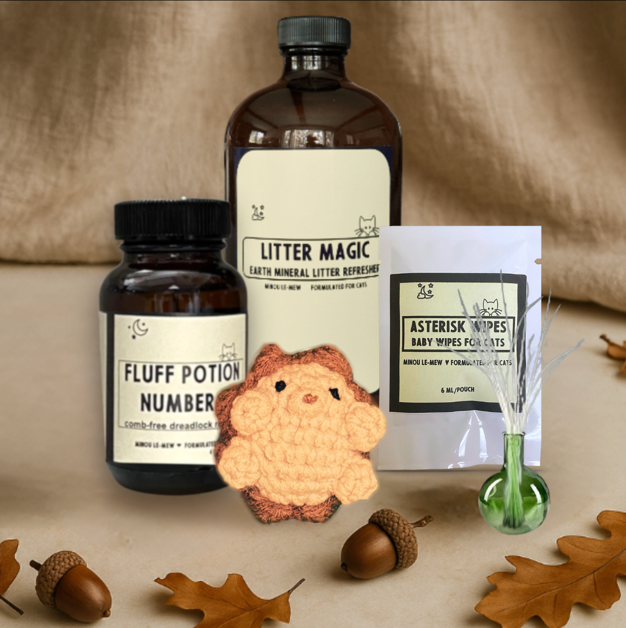 The Care Collection by Minou Le-Mew, featuring Asterisk Wipes, Litter Magic, a green glass Whisker Vase, Harold the Hedgehog Chunkle Puff, and Fluff Potion Number 9. A boutique set of cat care and play essentials designed for elegance and everyday ease.