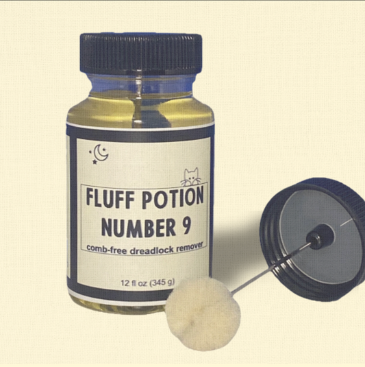 Fluff Potion Number 9, a 12 fl oz amber glass bottle with precision dauber cap by Minou Le-Mew, shown against a delicate cream colored backdrop. A luxury botanical no-comb mat remover for cats.