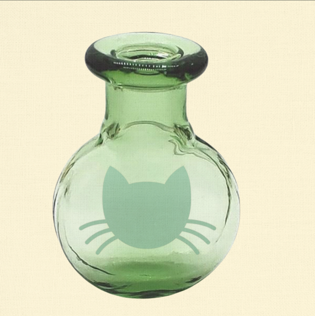 Closeup of a green round glass Whisker Vase with a foil cat face silhouette on the front, crafted for preserving and displaying whiskers.