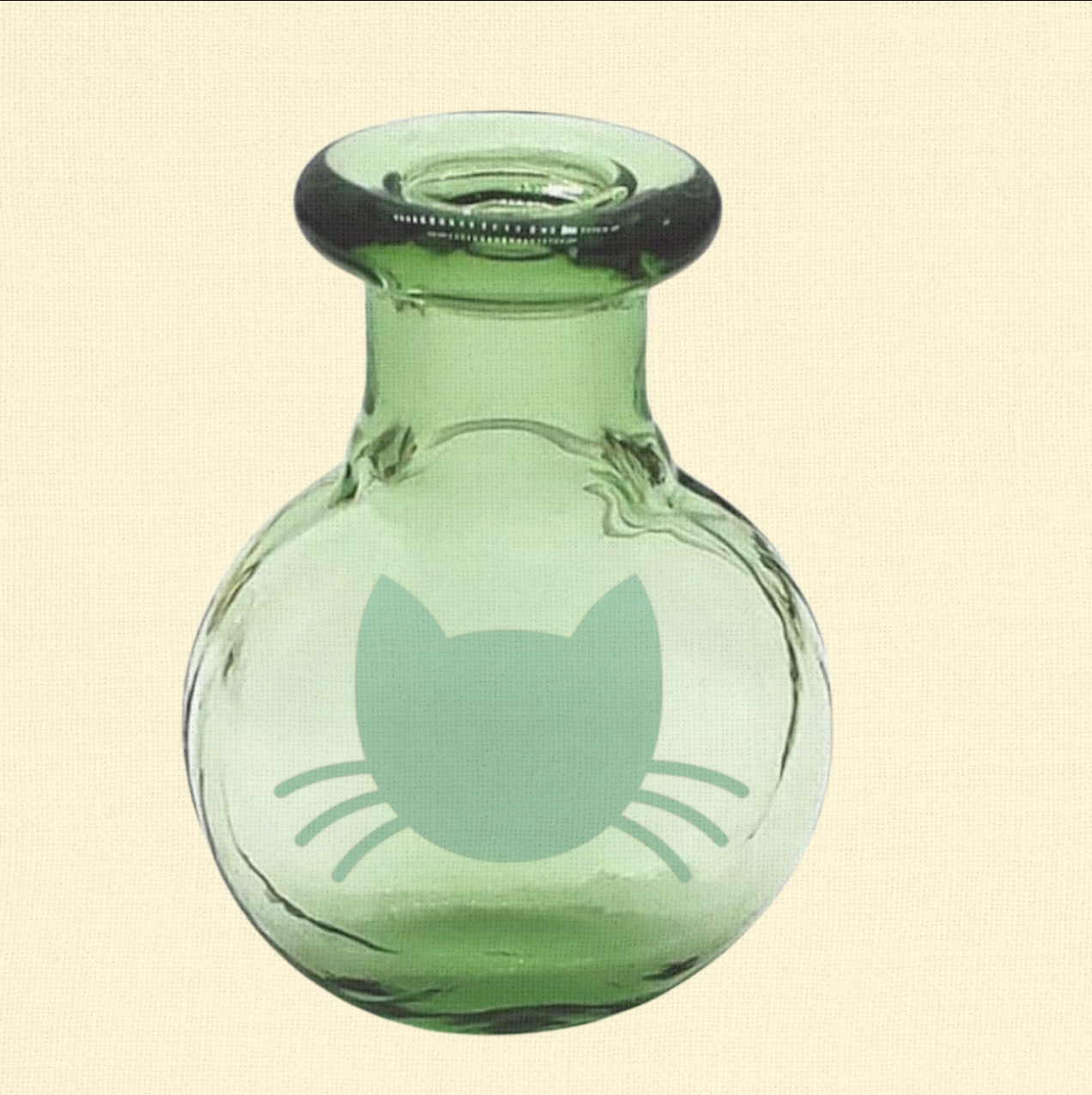 Closeup of a green round glass Whisker Vase with a foil cat face silhouette on the front, crafted for preserving and displaying whiskers.