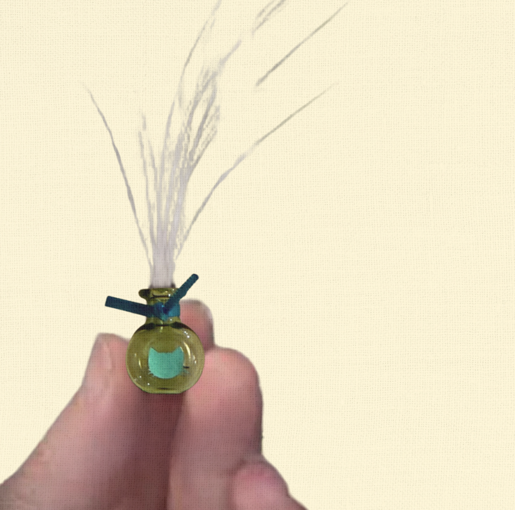 A green round glass Whisker Vase by Minou Le-Mew, featuring a foil cat silhouette, shown in a hand and filled with collected whiskers.