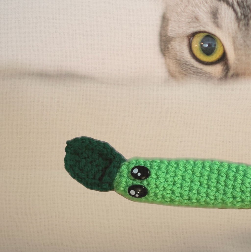 Noodle the Inchworm, a 3.5 inch handmade catnip toy, shown beside a cat's face for scale. The elongated Chunkle Puff form is designed for batting, carrying, and hiding.