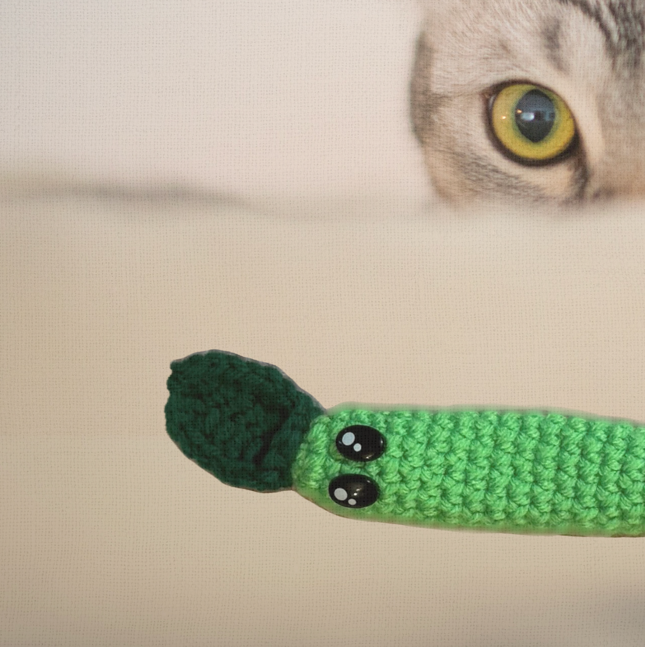 Noodle the Inchworm, a 3.5 inch handmade catnip toy, shown beside a cat's face for scale. The elongated Chunkle Puff form is designed for batting, carrying, and hiding.