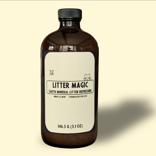 Litter Magic, an all-natural mineral litter refresher by Minou Le-Mew, shown in a 16 fl oz amber glass bottle with cream backdrop. A luxury cat care essential for fragrance-free odor control.