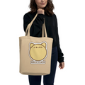 Person holding a beige tote bag with a cat graphic and text on a white background